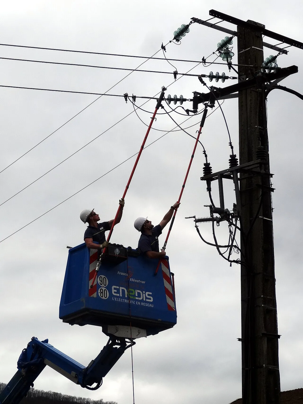 Een Enedis-technicus werkt vanuit een hoogwerker aan een middenspanningslijn, zoals bij het stormherstel in Frankrijk.